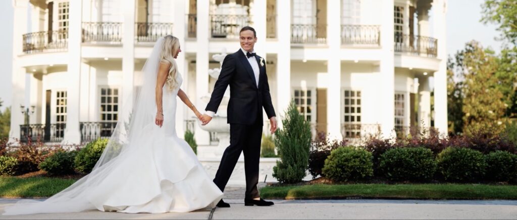 Couple walking hand in hand in front of their wedding venue, with the groom gazing lovingly at the bride as she walks beside him.