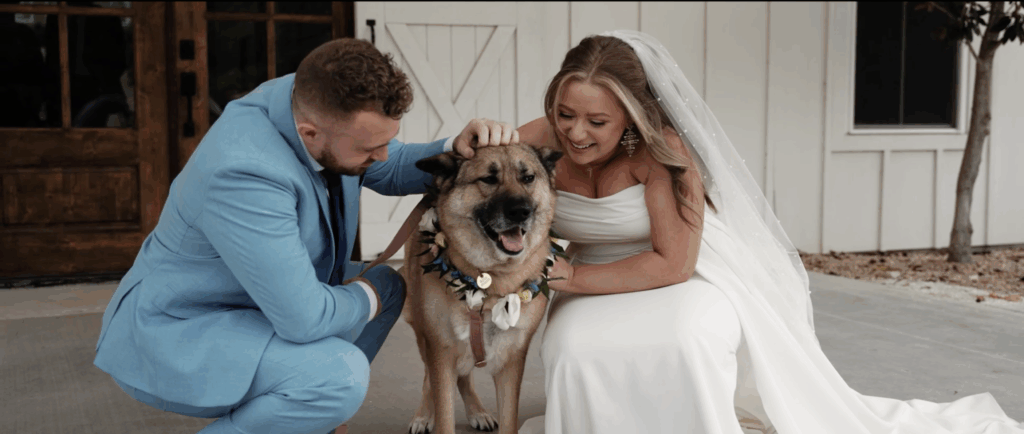 Bride and groom bend down to pet their dog outside of their wedding venue.
