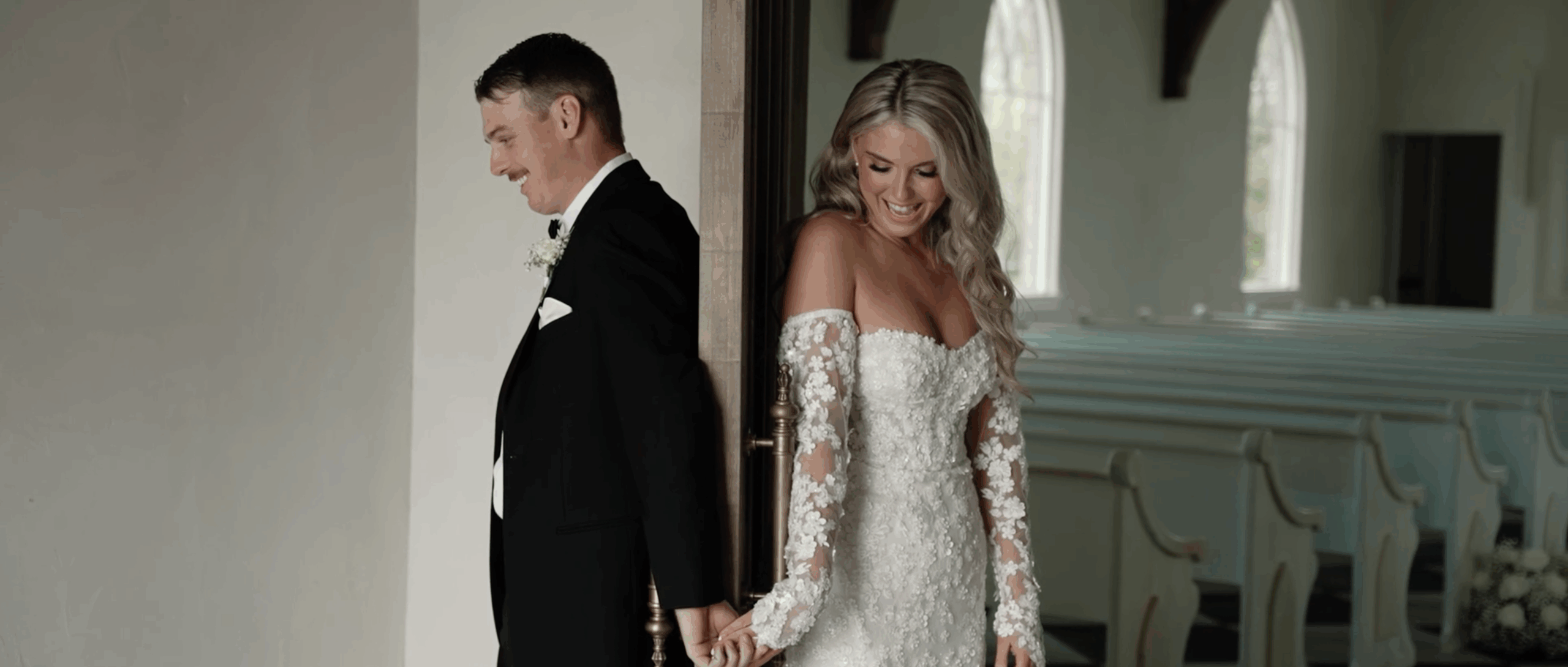 Bride and groom stand on opposite sides of a door, holding hands without seeing each other, sharing a quiet, emotional moment before the ceremony.