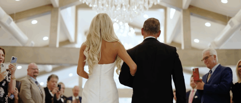 Bride walking down the aisle with her father, shown from behind, as they make their way toward the ceremony.