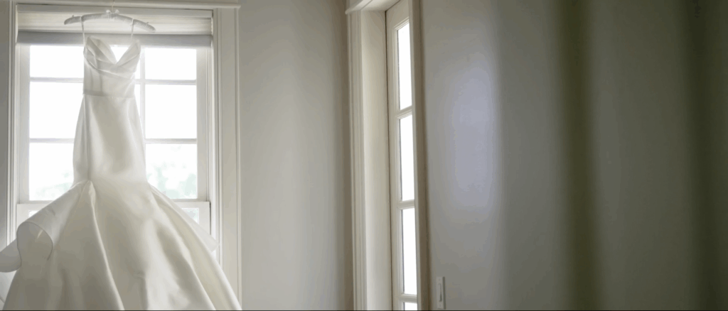 Wedding dress displayed hanging in a window, sunlight highlighting its fabric and details.