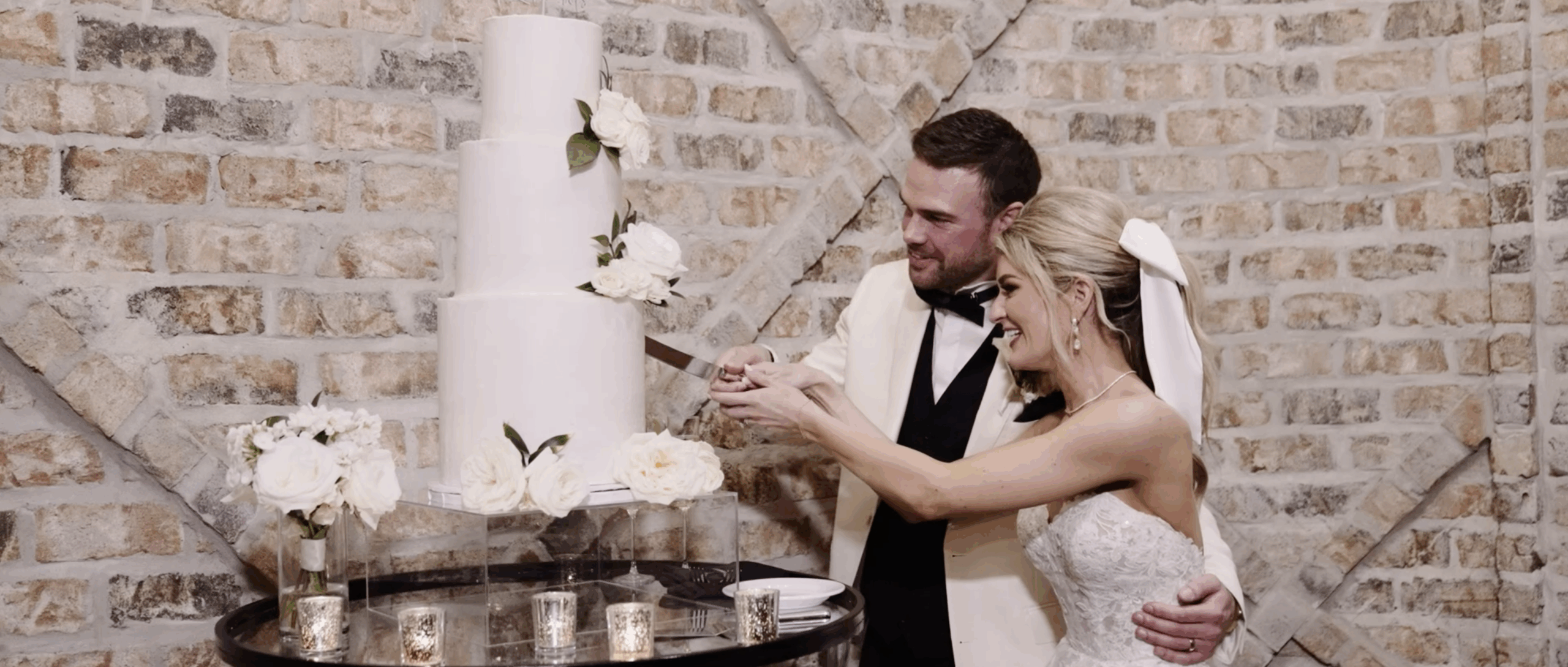 Bride and groom smiling as they cut their wedding cake together inside their reception space.