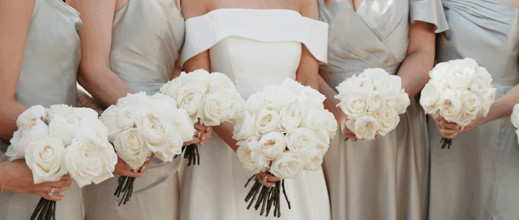 Close-up of bride and bridesmaids standing side by side, holding bouquets, with only their dresses and flowers visible.
