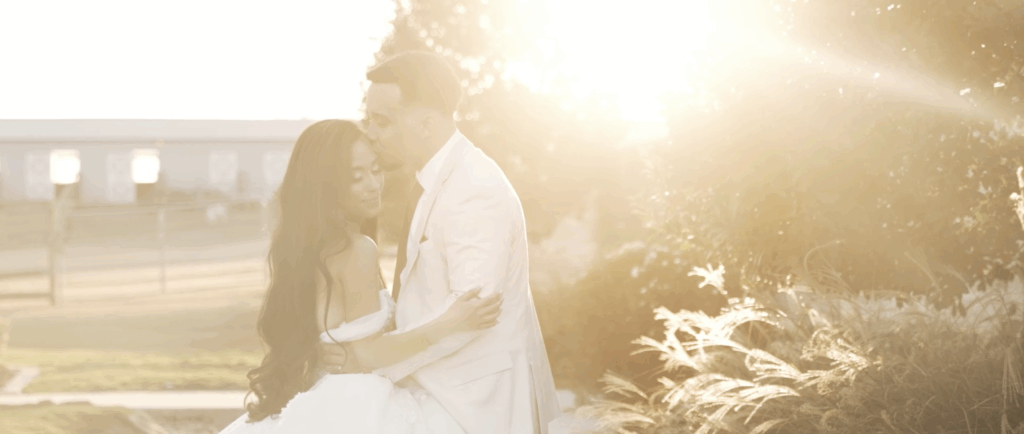 Groom gently kissing his bride on the forehead during golden hour, with warm sunlight creating a romantic glow.