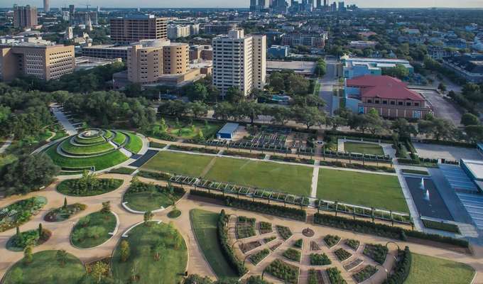 Aerial view of Hermann Park showing its gardens, large green spaces, winding pathways, and nearby Houston skyline.