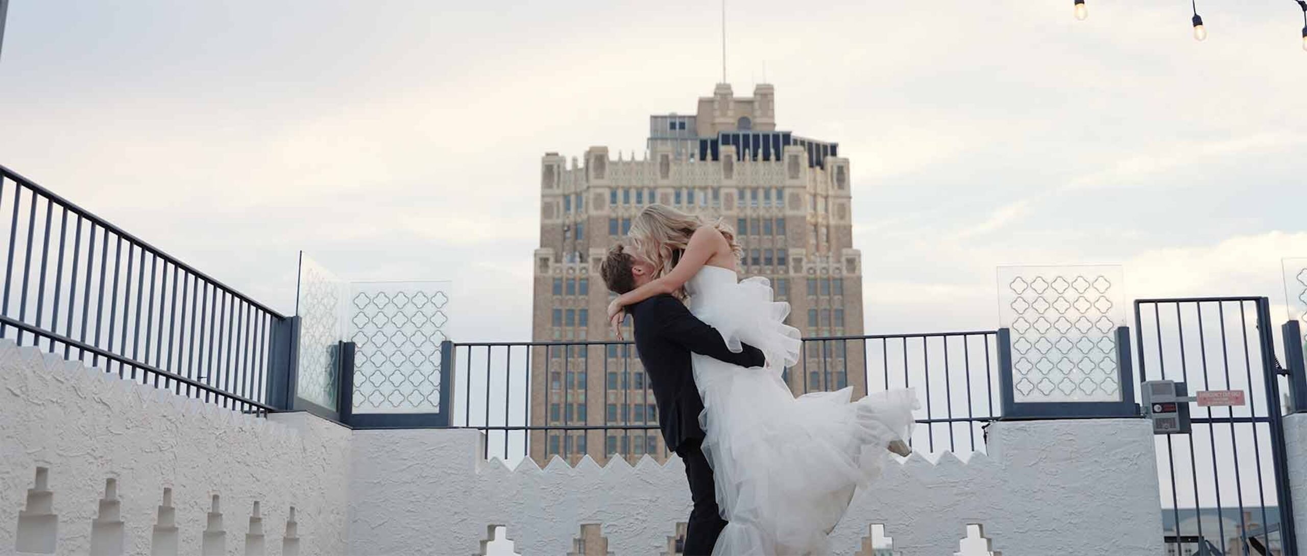Newlyweds kiss on the rooftop of their venue in the evening in Houston, TX.