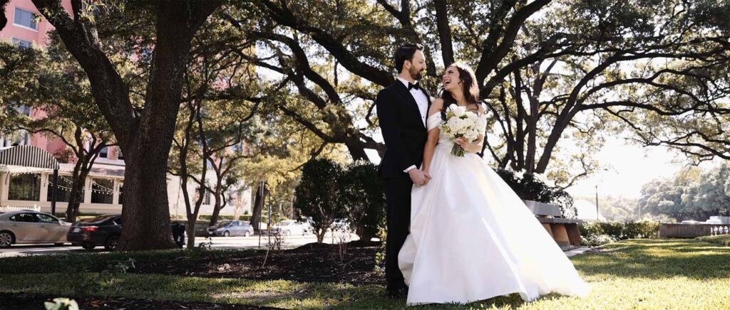 Bride glances back at her new groom while holding hands outside, capturing a joyful and romantic post-ceremony moment.