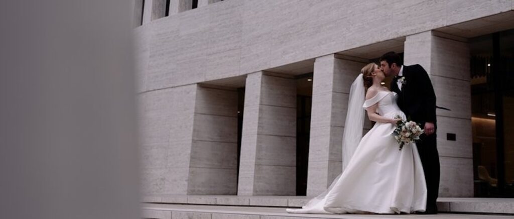 Bride and groom share a romantic kiss in front of a building, capturing an elegant and timeless wedding moment.