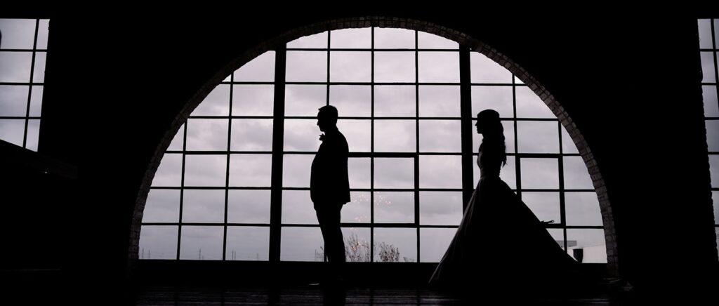 A bride and groom in front of a large window for a beautiful silhouette in a wedding hall.