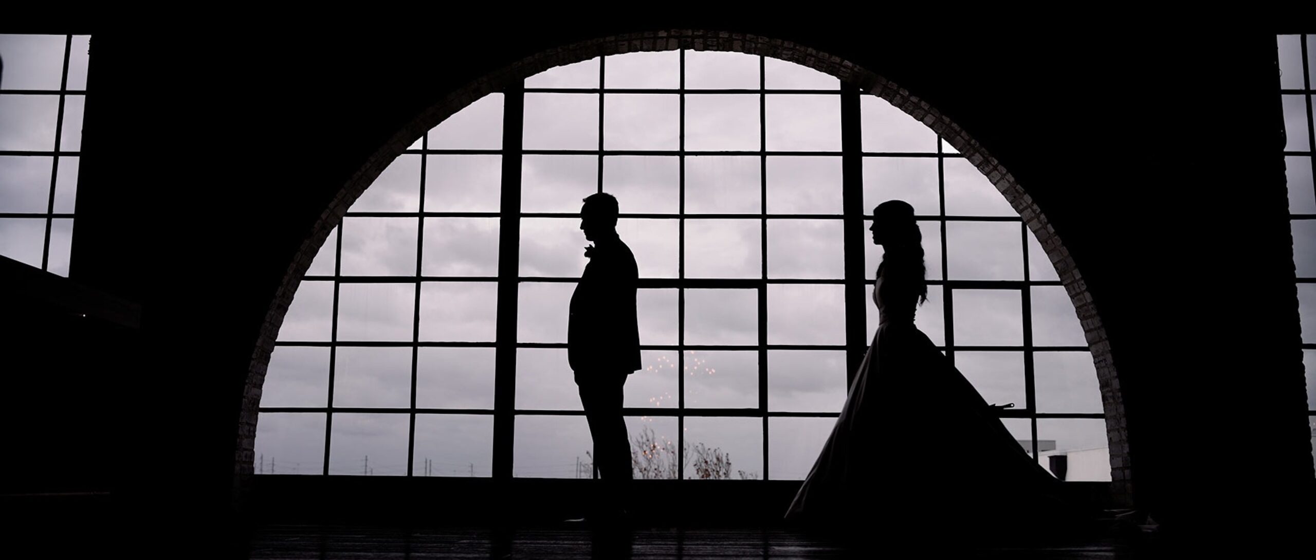 A bride and groom in front of a large window for a beautiful silhouette in a wedding hall.