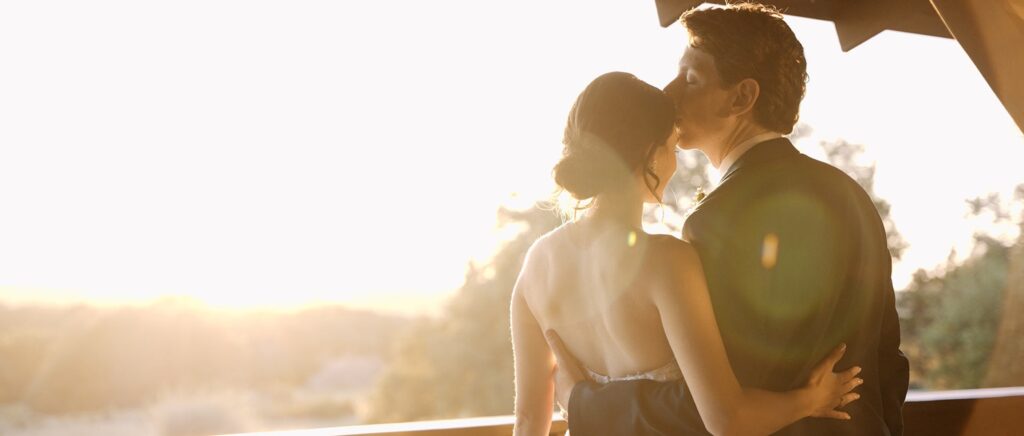 Groom kisses his bride as they look over the porch at their Dallas wedding venue.